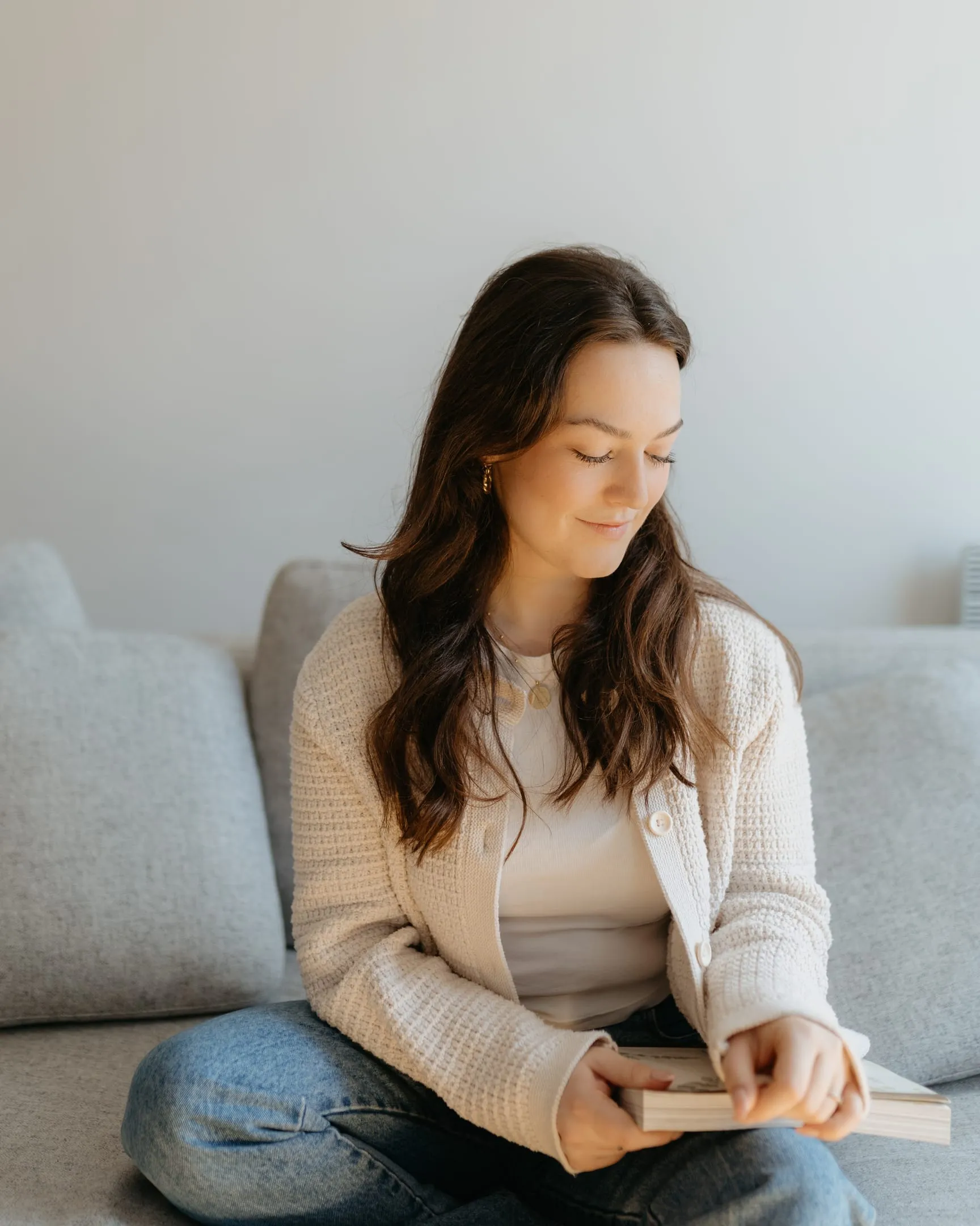 Daphné feuilletant un livre, assise en tailleur sur un divan clair
