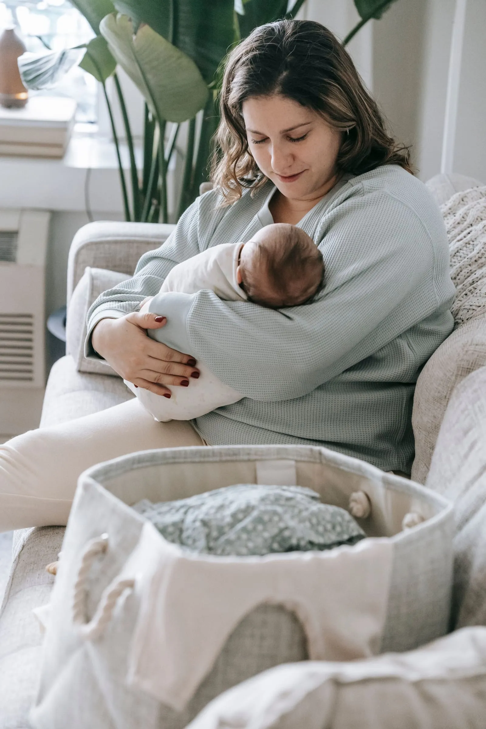 Mère assise sur un divan beige, son nouveau-né endormi dans les bras