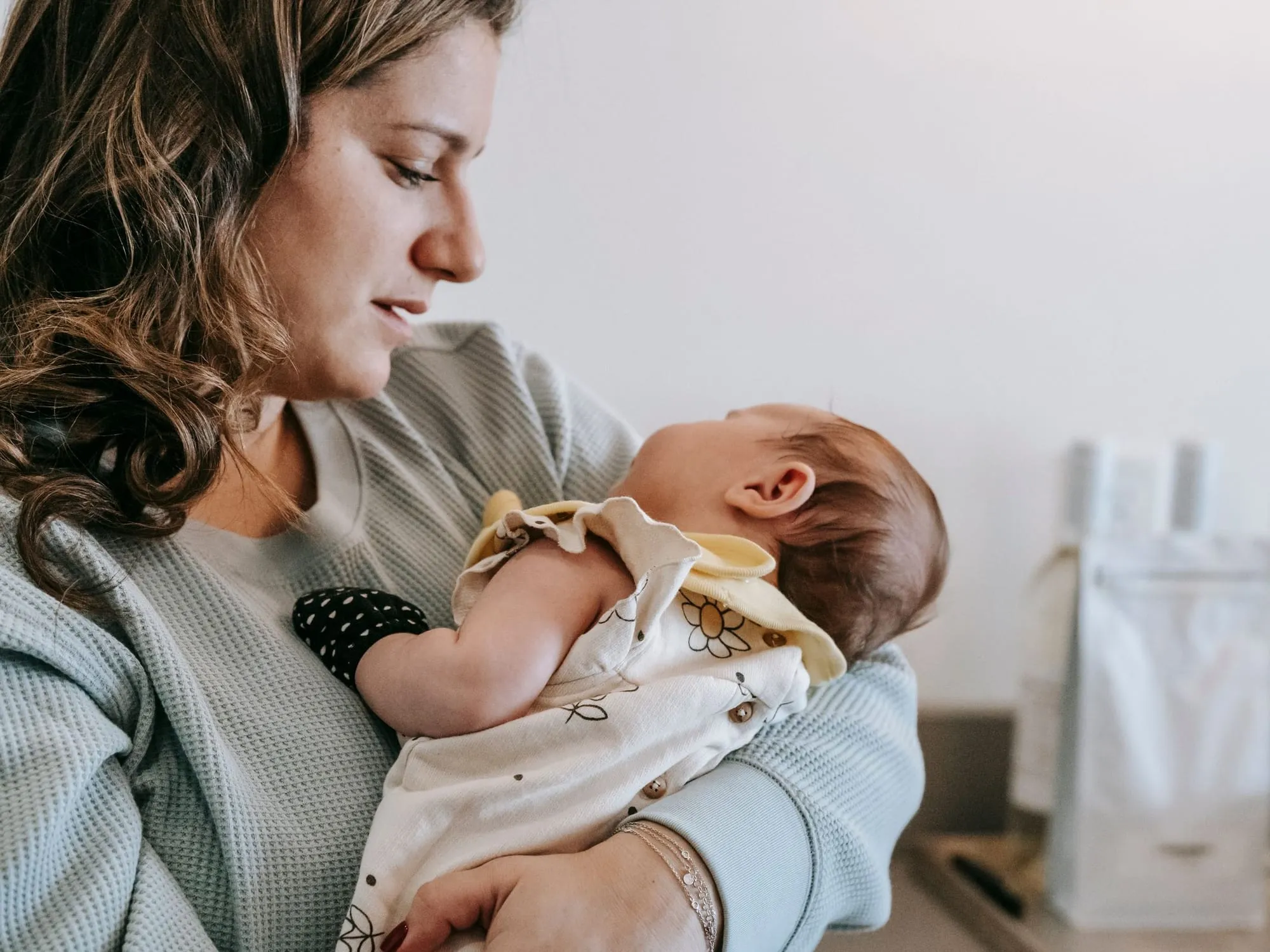 Mère en tricot sauge berçant son nouveau-né dans une pièce claire aux tons crème